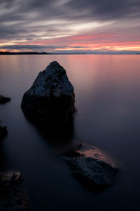 Rocks in sea against sky during sunset