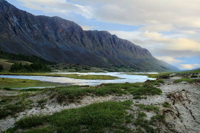 Alpine valley with river, grass, trees and a huge mountain range at sunset