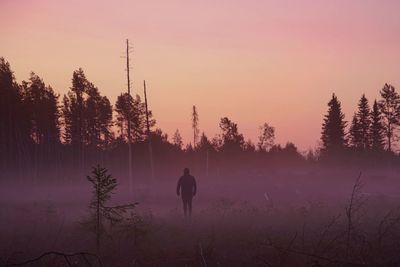 Silhouette person standing by trees in forest against sky during sunset