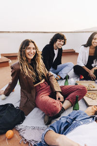 Portrait of smiling woman sitting cross-legged with male and friends during party on rooftop