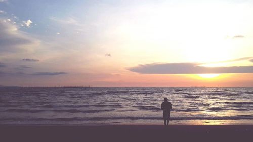 Silhouette person standing on beach against sky during sunset