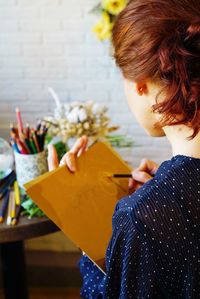 Close-up of woman drawing on paper against brick wall