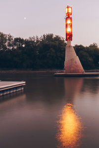 Illuminated built structure by lake against sky at night