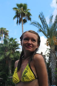 Portrait of woman standing by palm trees against sky