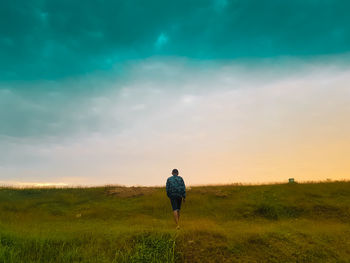 Rear view of man on field against sky during sunset