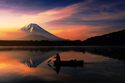 Silhouette man on boat sailing lake against dramatic sky