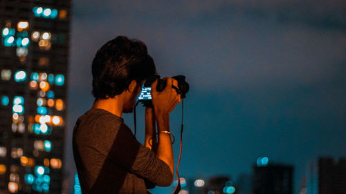 Teenage boy photographing with camera in city at night