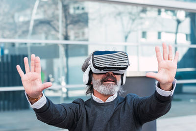 Amazed senior man using vr headset outdoor the office building, modern technologies experience