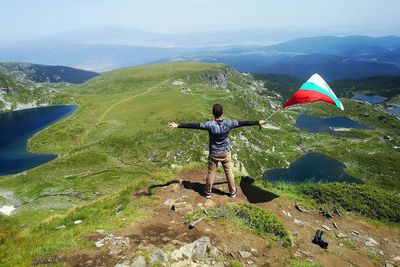 Rear view of man with arms outstretched holding flag while standing on mountain