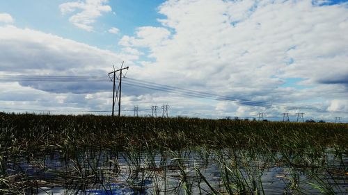 Electricity pylon on field against cloudy sky