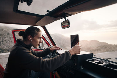 Side view of man with wireless in-ear headphones using laptop while sitting in van on vacation