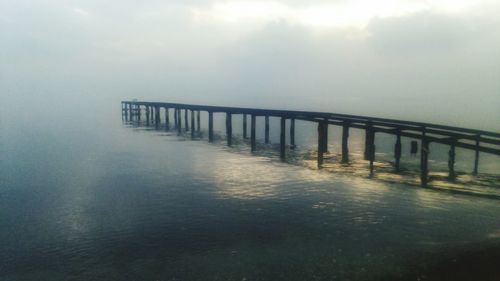 Pier on sea against cloudy sky