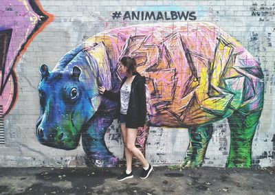 Full length of woman standing against graffiti wall