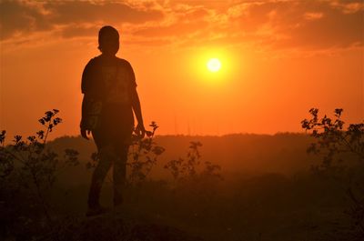 Rear view of silhouette man standing on field against sky during sunset