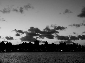 Silhouette city by sea against sky