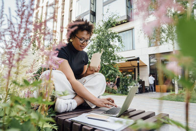 Businesswoman with take out food box using laptop sitting on bench