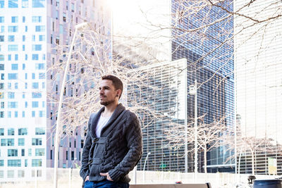 Young man looking away against buildings in city