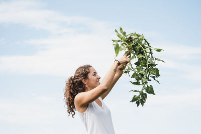 Woman holding plant against sky