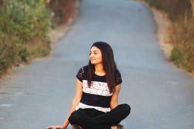 Young woman looking away while sitting on road