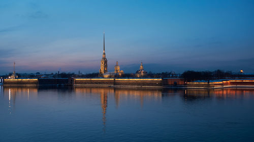 Illuminated buildings by river against sky in city