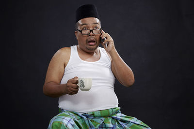 Shocked man with coffee using phone against black background