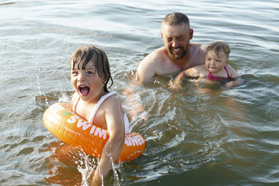 The boy swims with swimming circle and girl swims with daddy