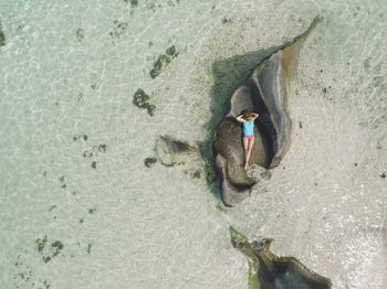 Drone shot of woman relaxing on rock at beach