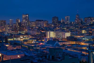 Illuminated cityscape against blue sky at night