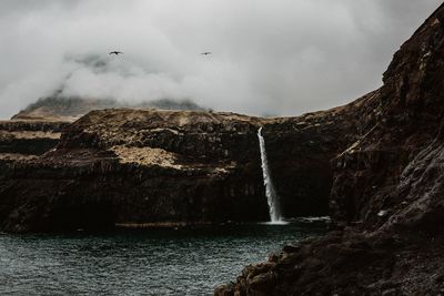 Scenic view of waterfall against cloudy sky