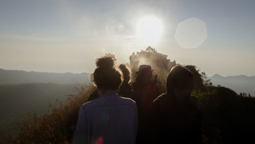 Rear view of people standing on mountain against sky