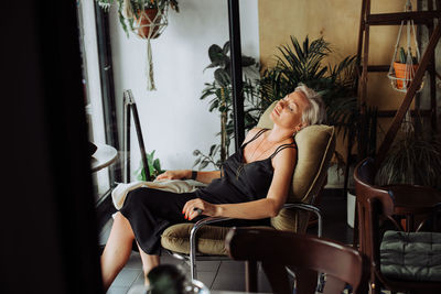 Blond woman in black dress sitting alone in cafe in relaxed position