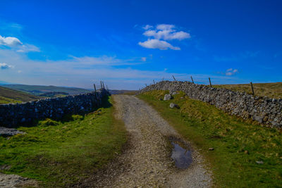 Road amidst field against blue sky