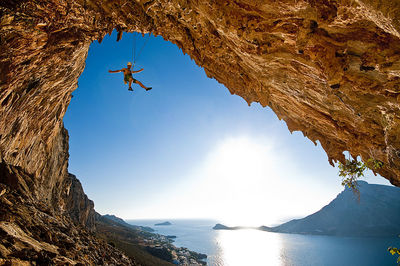 Low angle view of man climbing rock by lake against sky