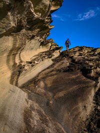 Low angle view of man climbing on rock against sky