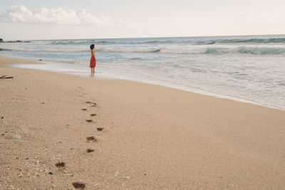 Side view of woman standing at beach against sky