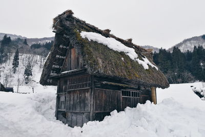 Snow covered house by building against sky