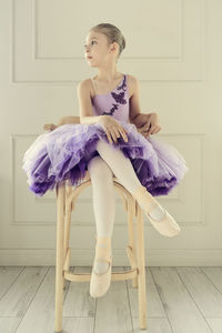 A portraits of a ballerina girl in a lilac dress sitting on a chair