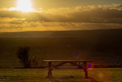 Empty bench and table against sky during sunset