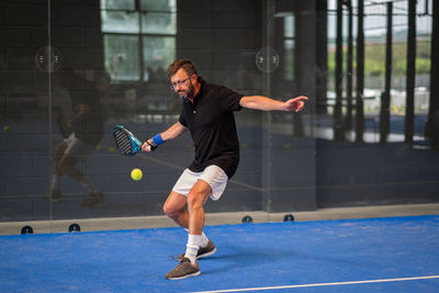Man playing padel in a blue grass padel court indoor - young sporty boy padel player hitting ball 
