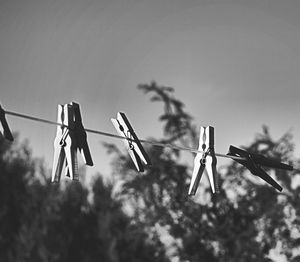 Low angle view of clothespins hanging on rope against sky