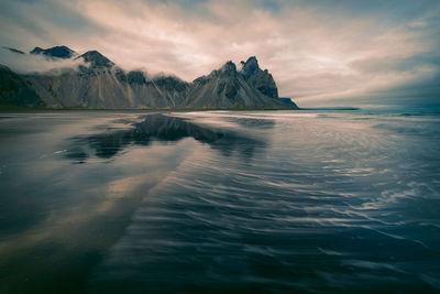 Scenic view of sea by mountains against sky during sunset