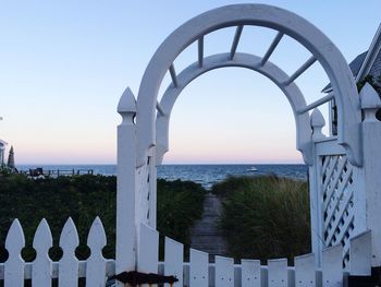 Sea seen through arch fence against sky during sunset