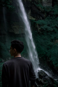 Rear view of man looking at waterfall in forest