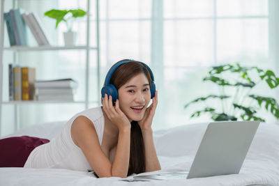Smiling young woman using mobile phone in bed