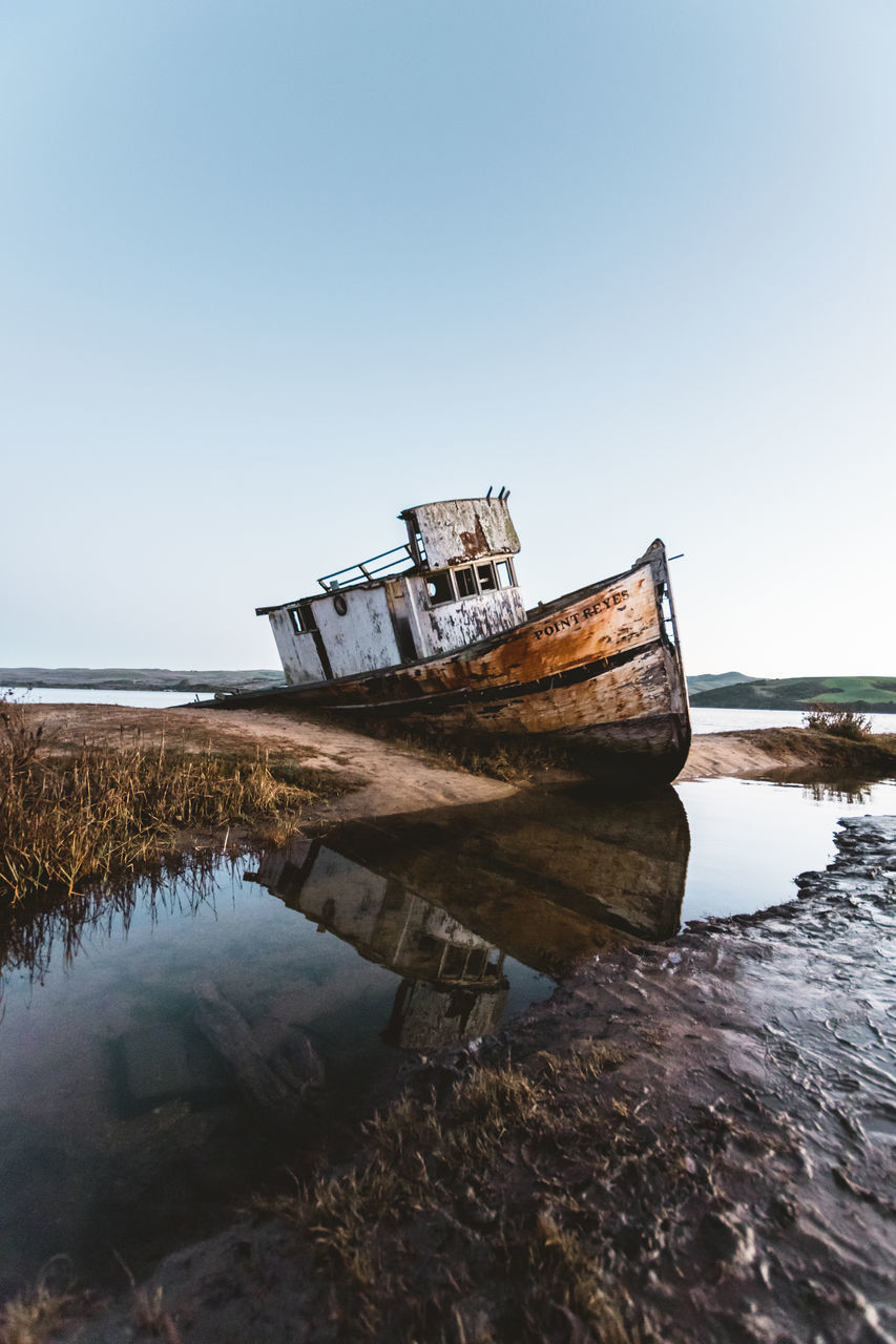 ABANDONED BOAT ON SHORE AGAINST CLEAR SKY