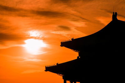 Low angle view of silhouette building against orange sky