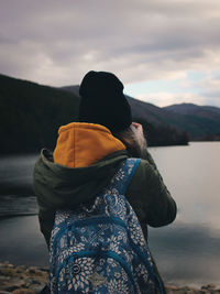 Rear view of woman standing by lake against sky