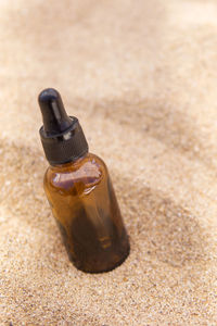 Cosmetic serum in a glass bottle with a pipette in the sand