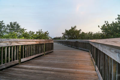 Wooden footbridge along plants and trees against sky