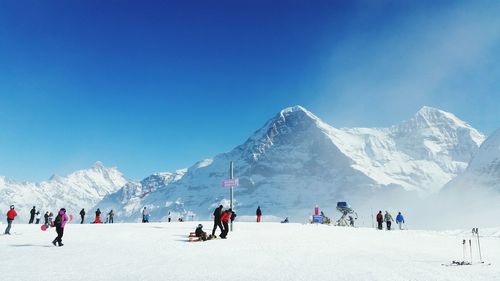 Panoramic view of people on snowcapped mountain against blue sky